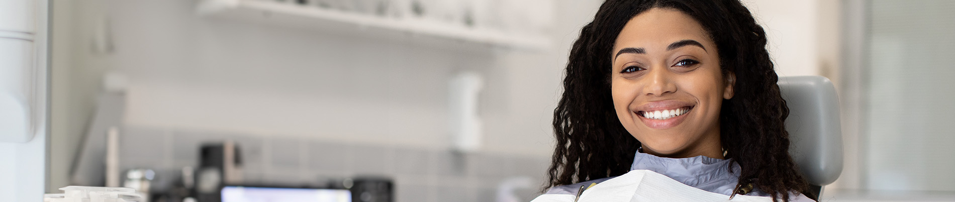 A person is seated in a dental chair, receiving care from a dental professional who stands behind them.